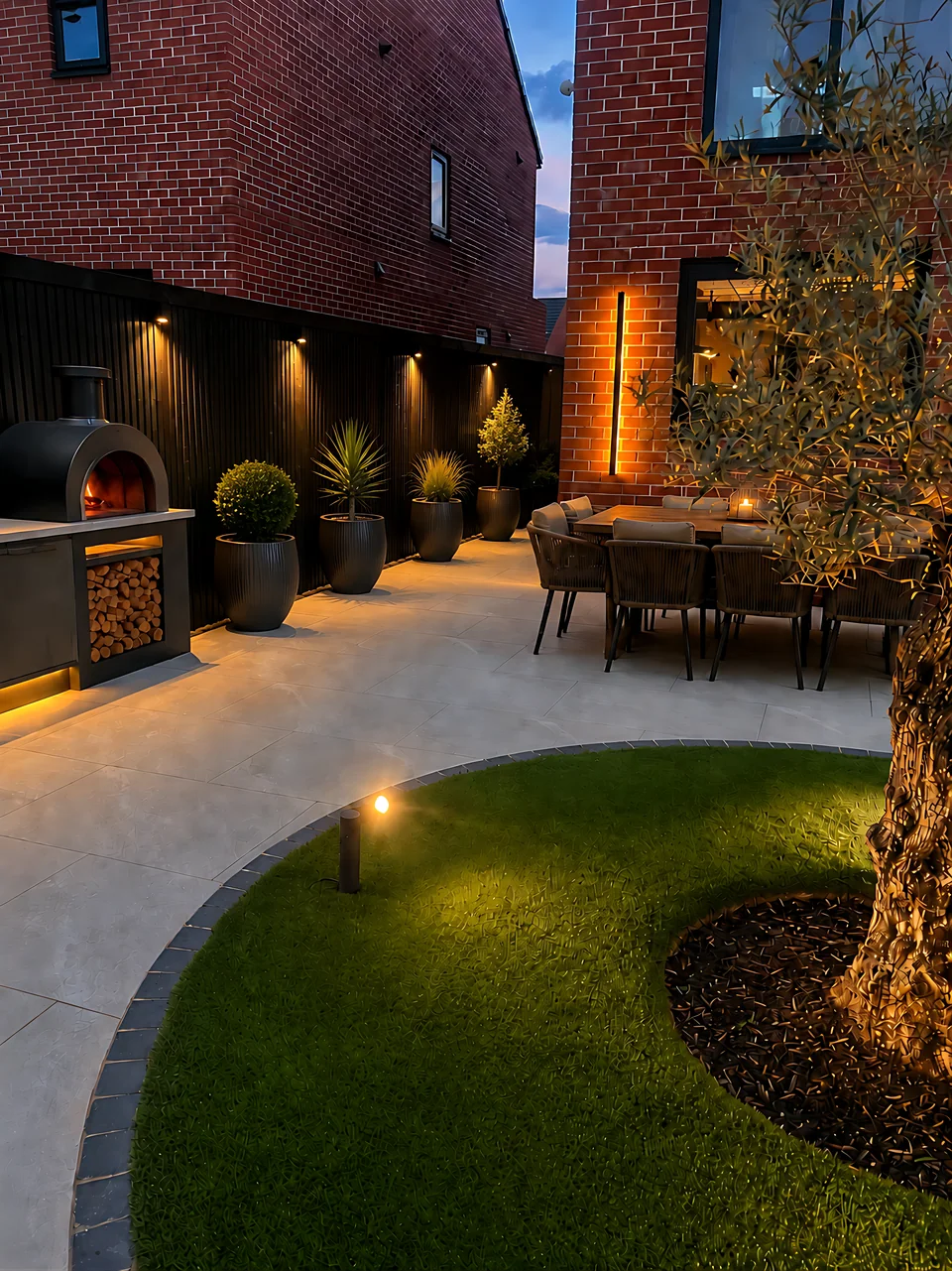 A contemporary garden at dusk with a curved lawn and lit fencing